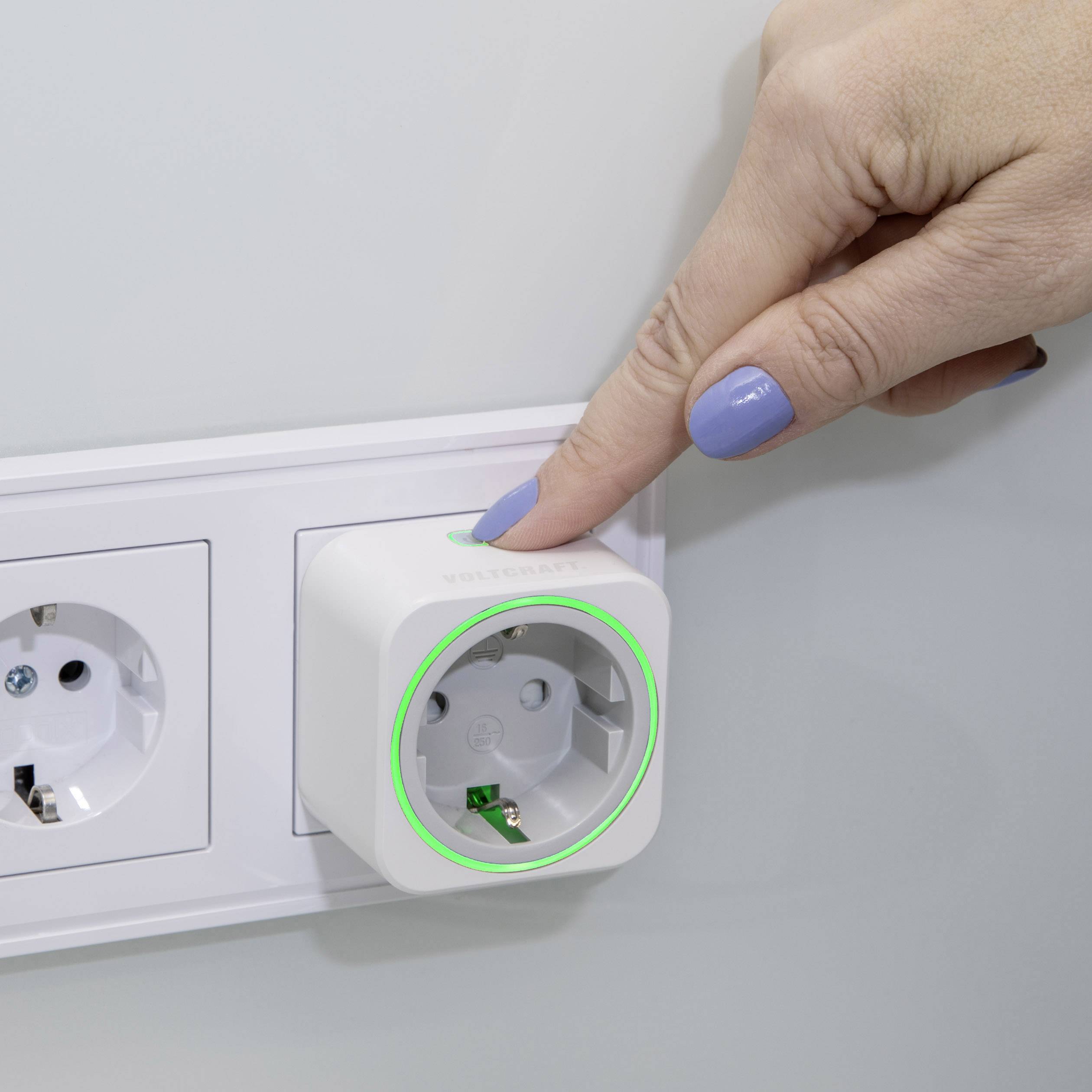 A hand presses the switch of a digital socket on the wall to turn a device on or off.