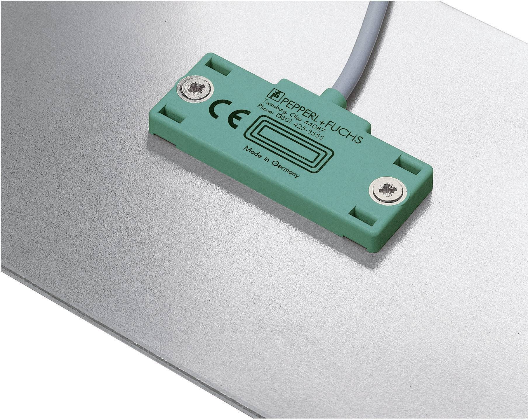 A green sensor with the inscription 'Pepperl+Fuchs', CE marking and 'Made in Germany'. Mounted on a metal surface.