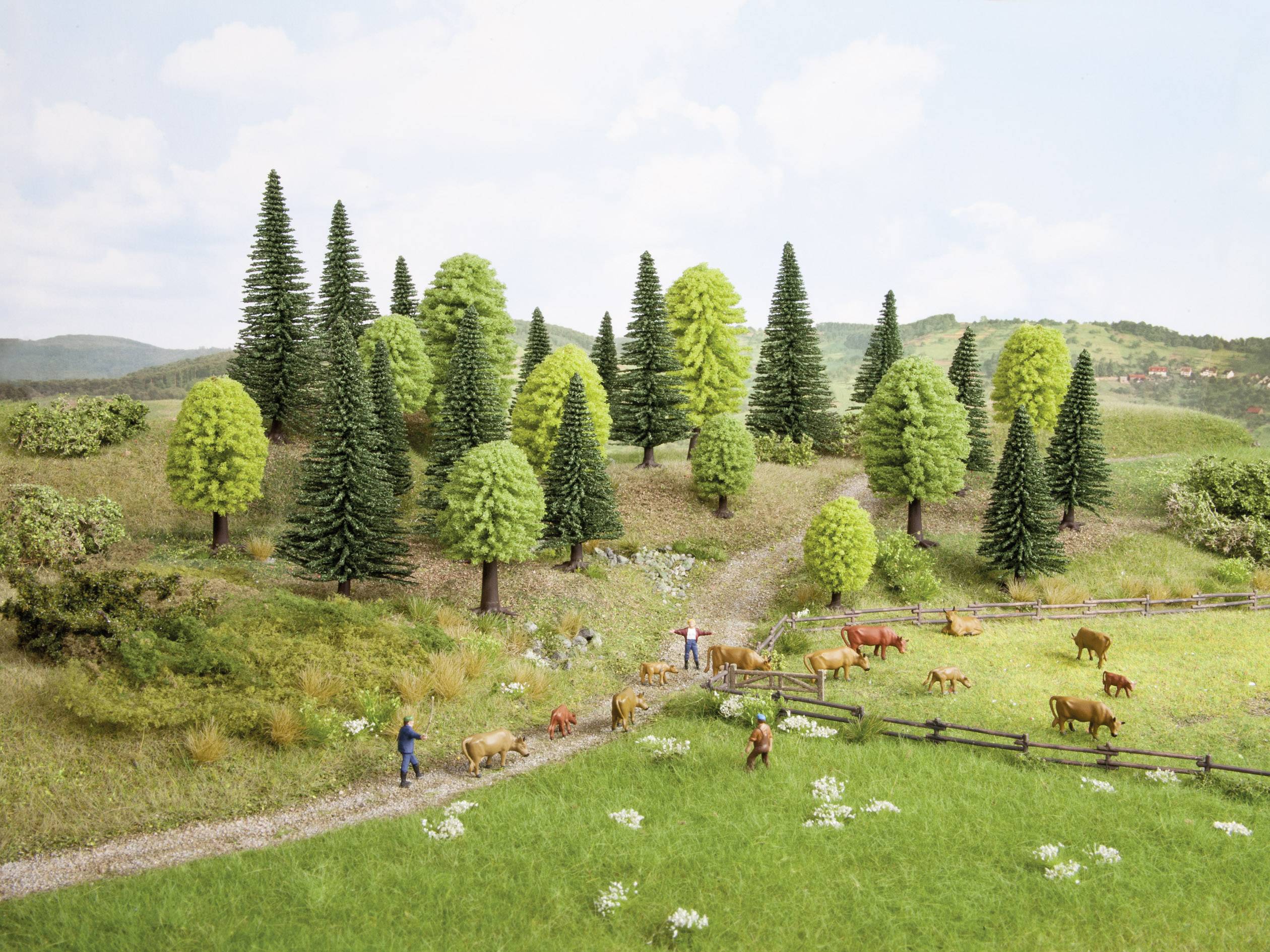 Landscape of green hills, numerous trees and a pasture with cows. Two people are walking along a path beside the cows.