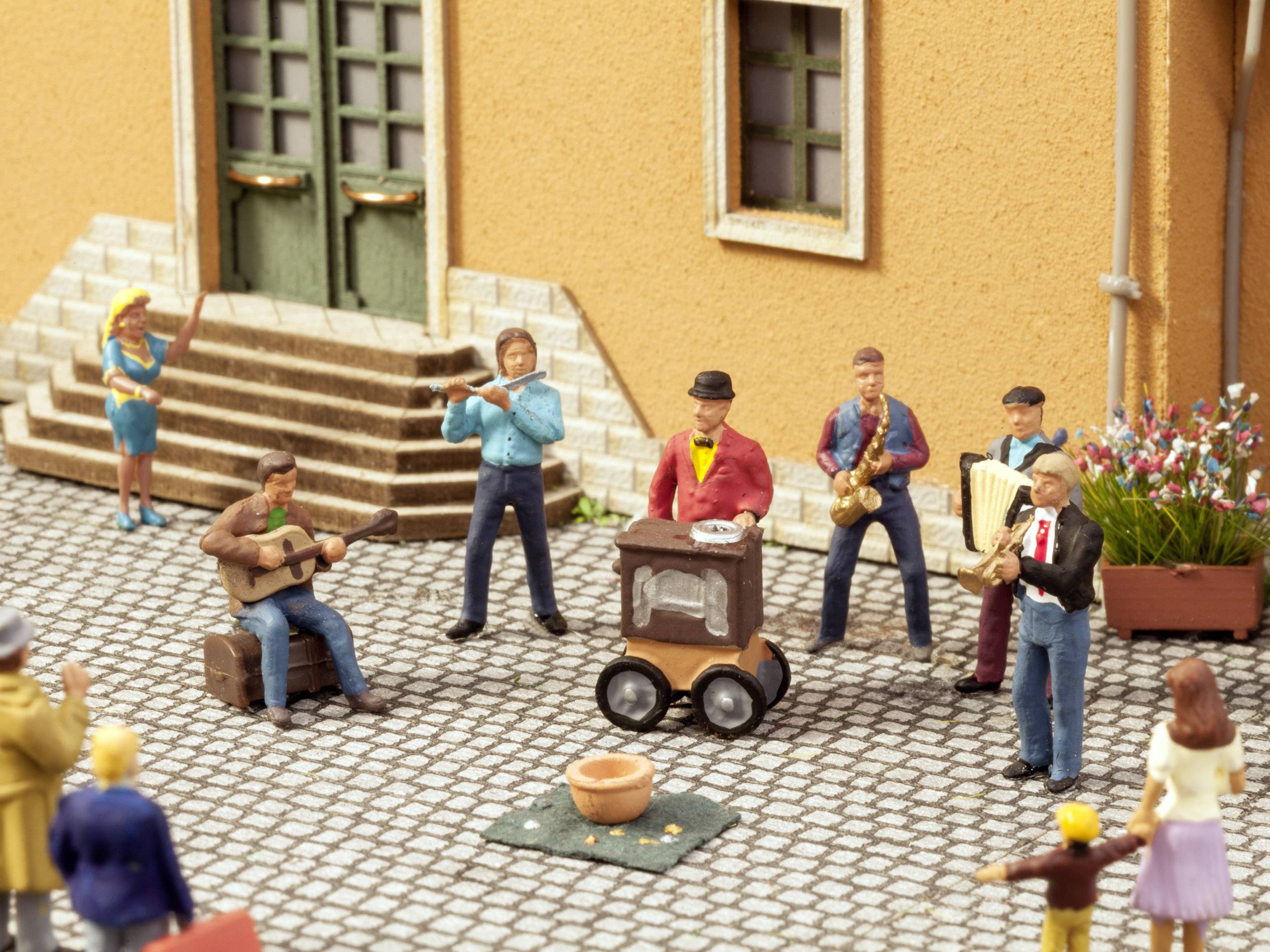 Street scene with miniature figures: Musicians playing guitar, flute, trumpet and accordion, while a woman dances.