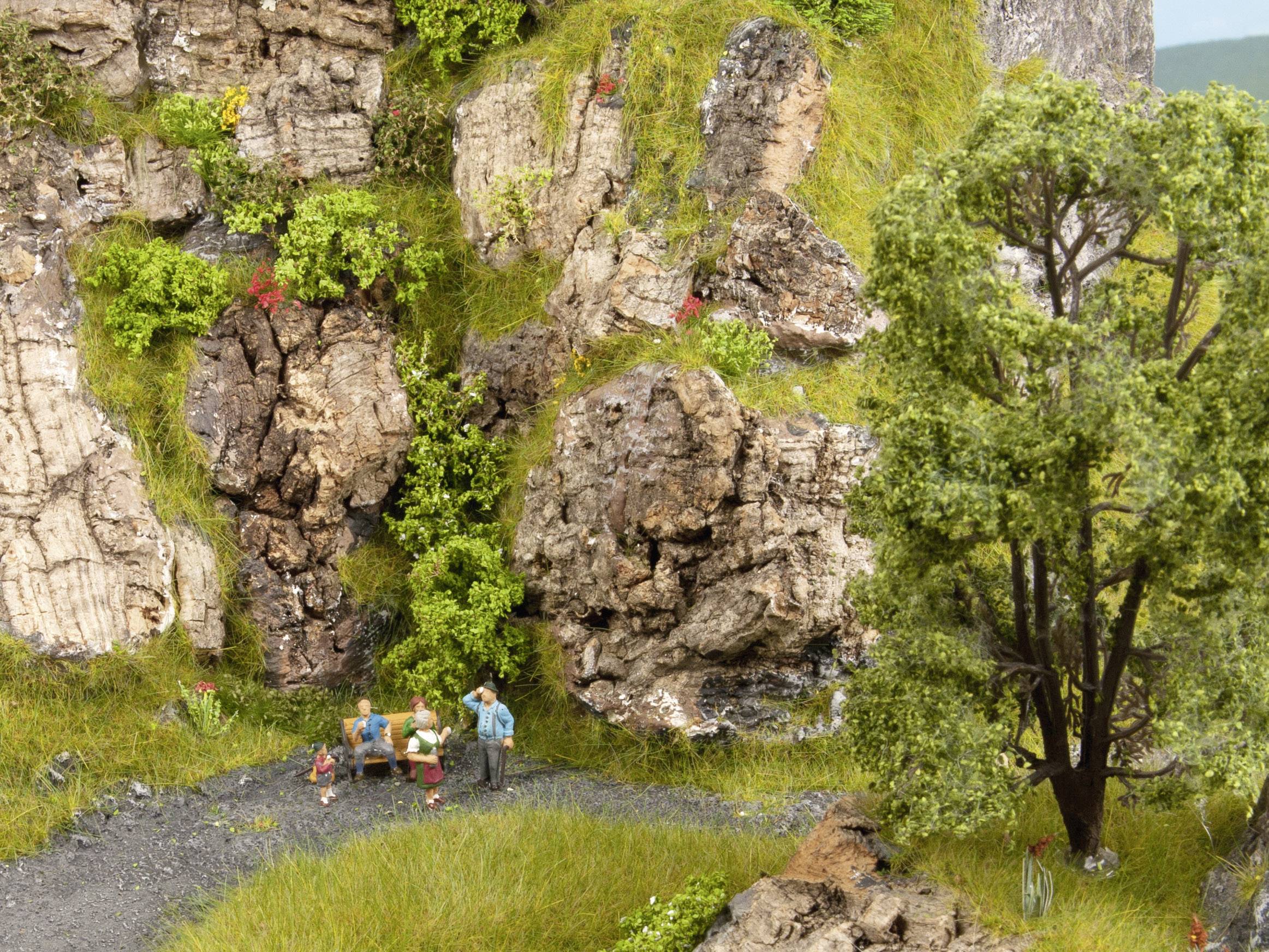 Small-scale scene: Four people are hiking along a path beside steep rocks and green trees, surrounded by lush moss and grass.