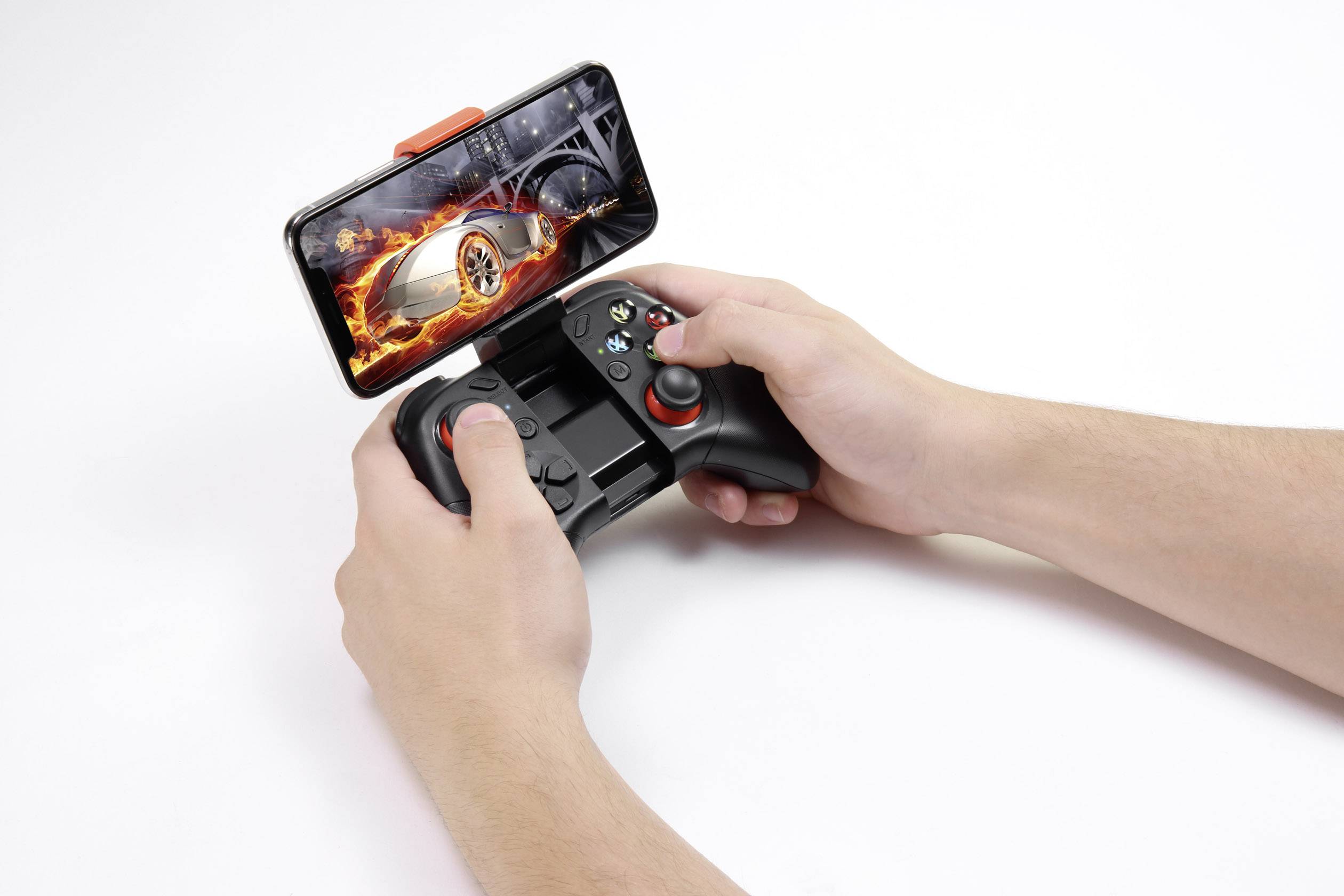 A person is holding a game controller with a smartphone inserted. On the screen, a car racing game featuring a burning car is displayed.