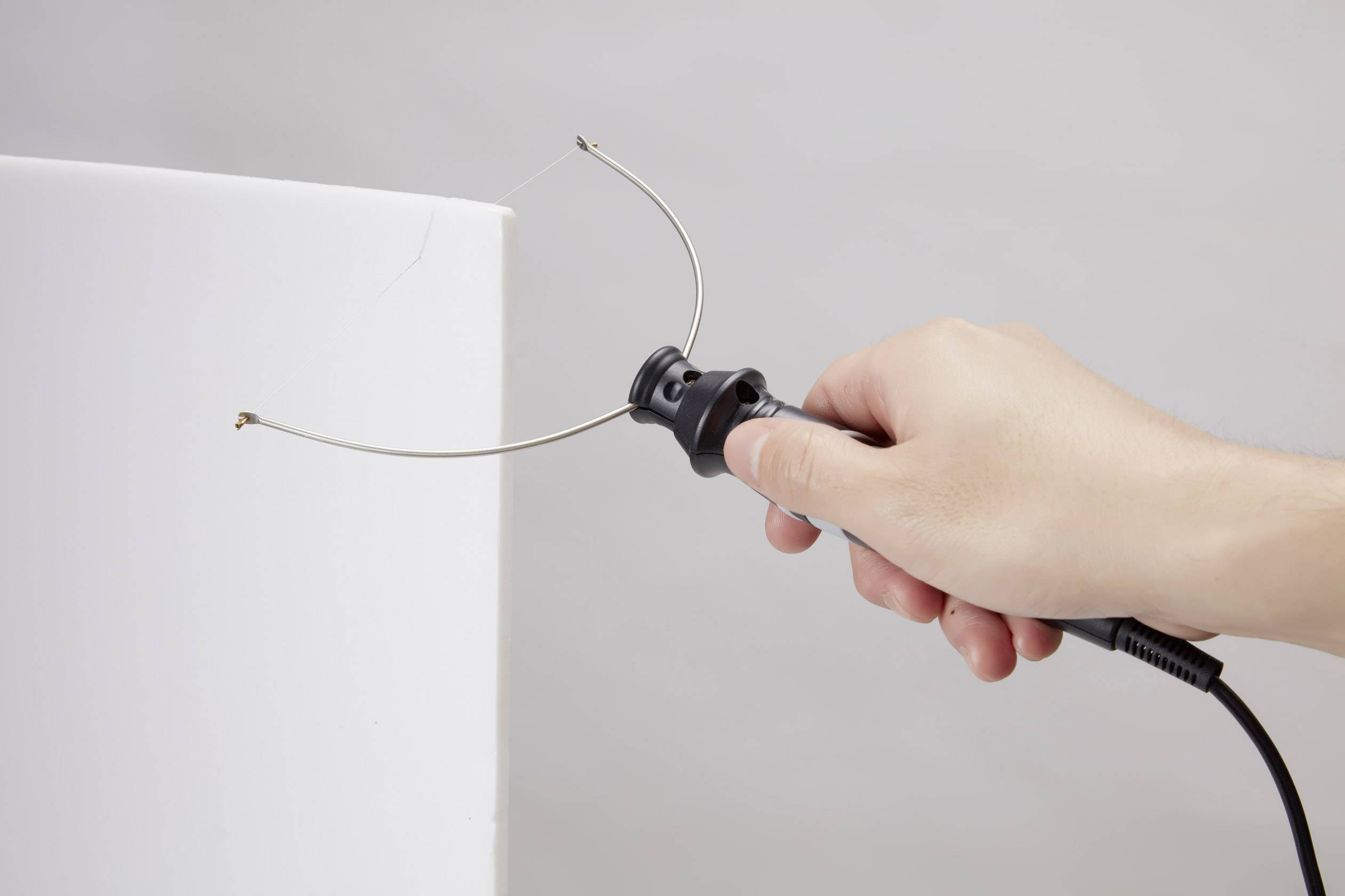 A hand is holding a tool with a curved wire, pointed at a white block, presumably for cutting or shaping.