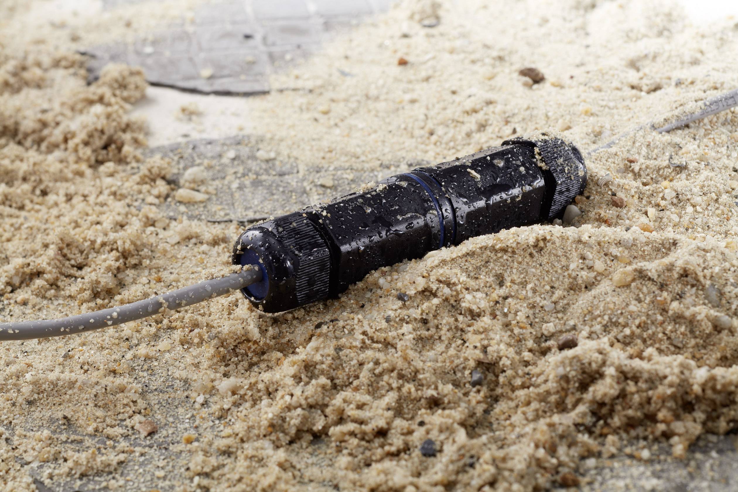 A black cable lies on sandy ground, partially covered by sand, which indicates a rough or unprotected environment.