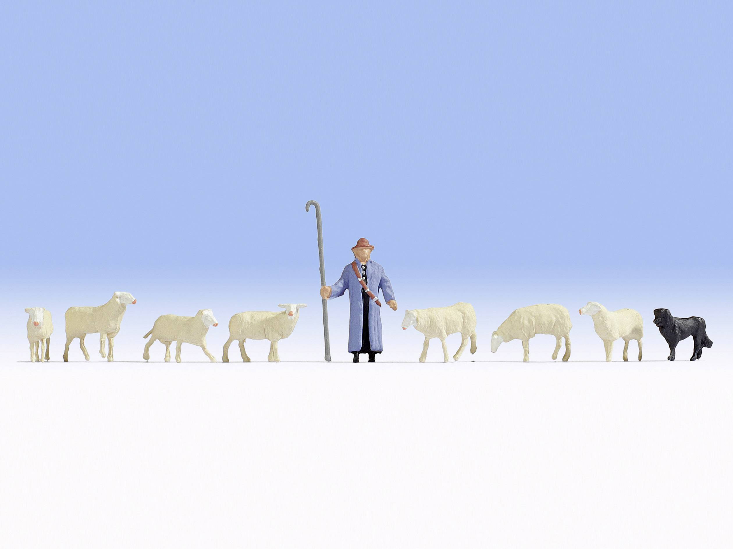 A shepherd in blue clothing and a hat stands with a sheepdog and seven sheep on an open field under a clear sky.