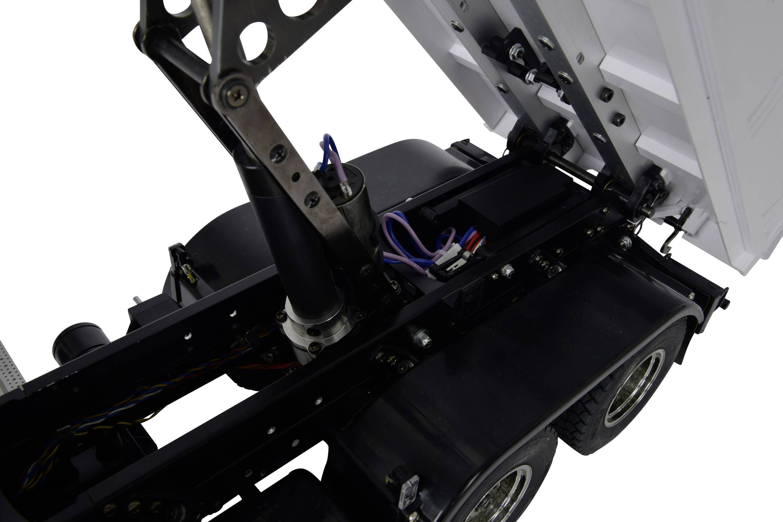Close-up of a model lorry chassis with visible electronics and mechanics. The cab is raised, revealing cables and drive structure.