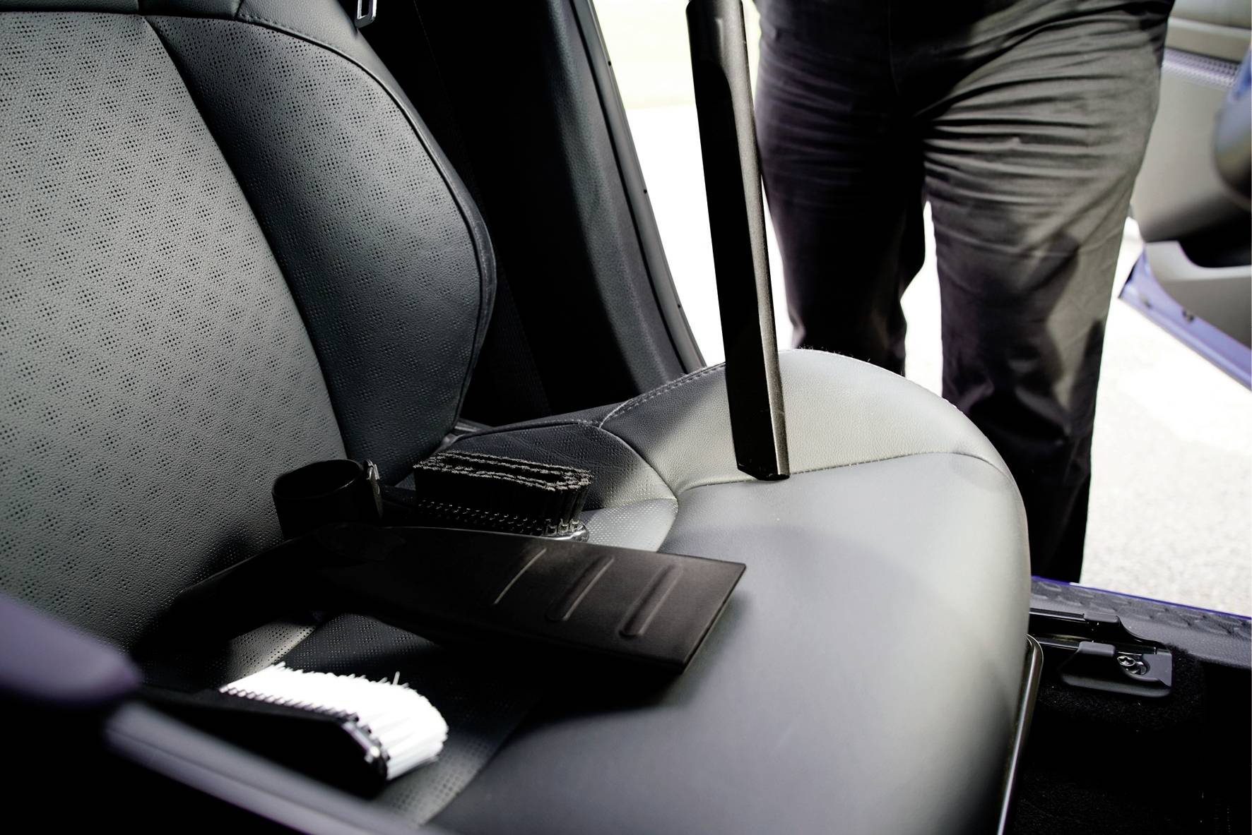 A person is standing next to an open car door, with the seat belt lying on the front seat.