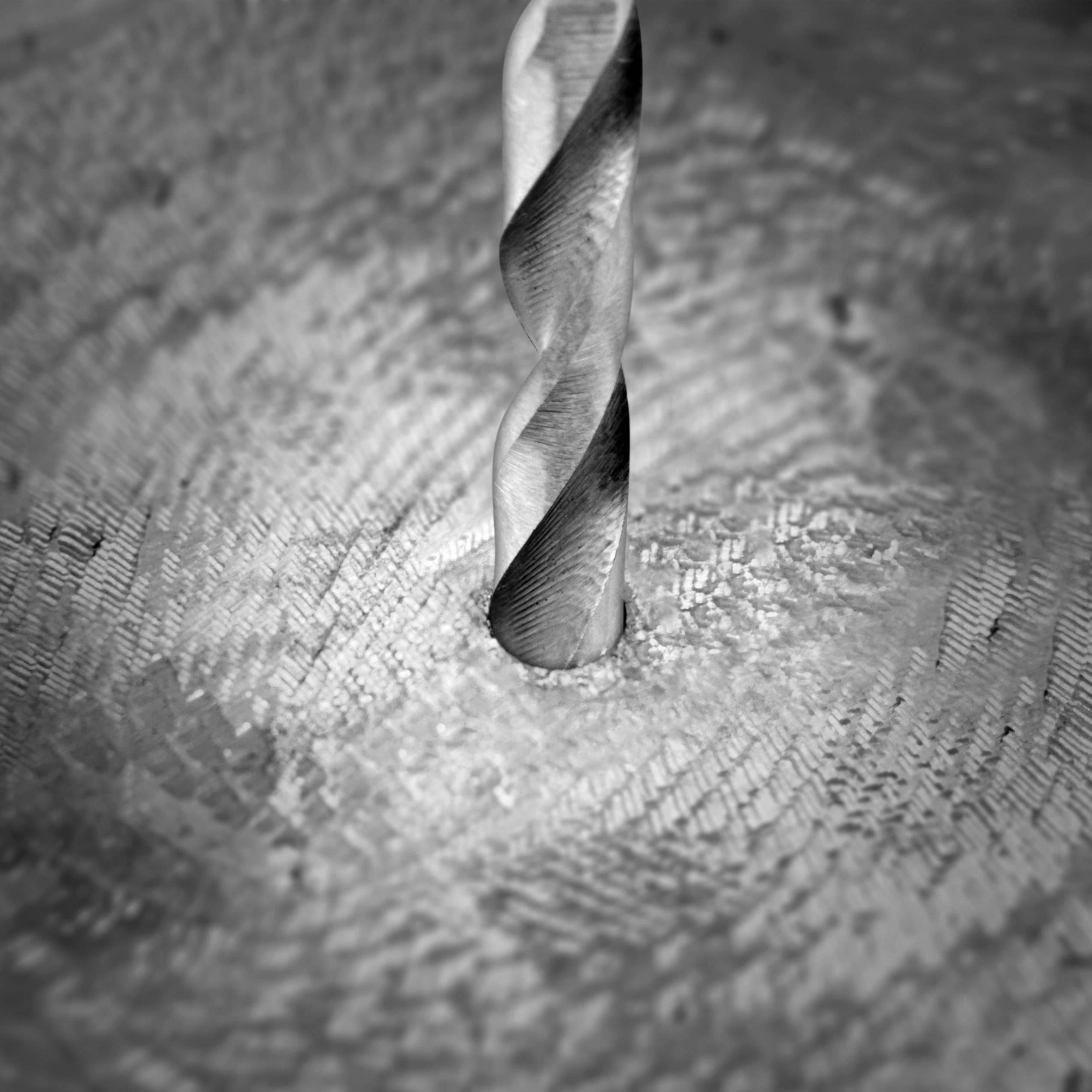 Close-up of a drill bit boring into a metal surface, with metal shavings and texture in the background. Creating metal spirals.