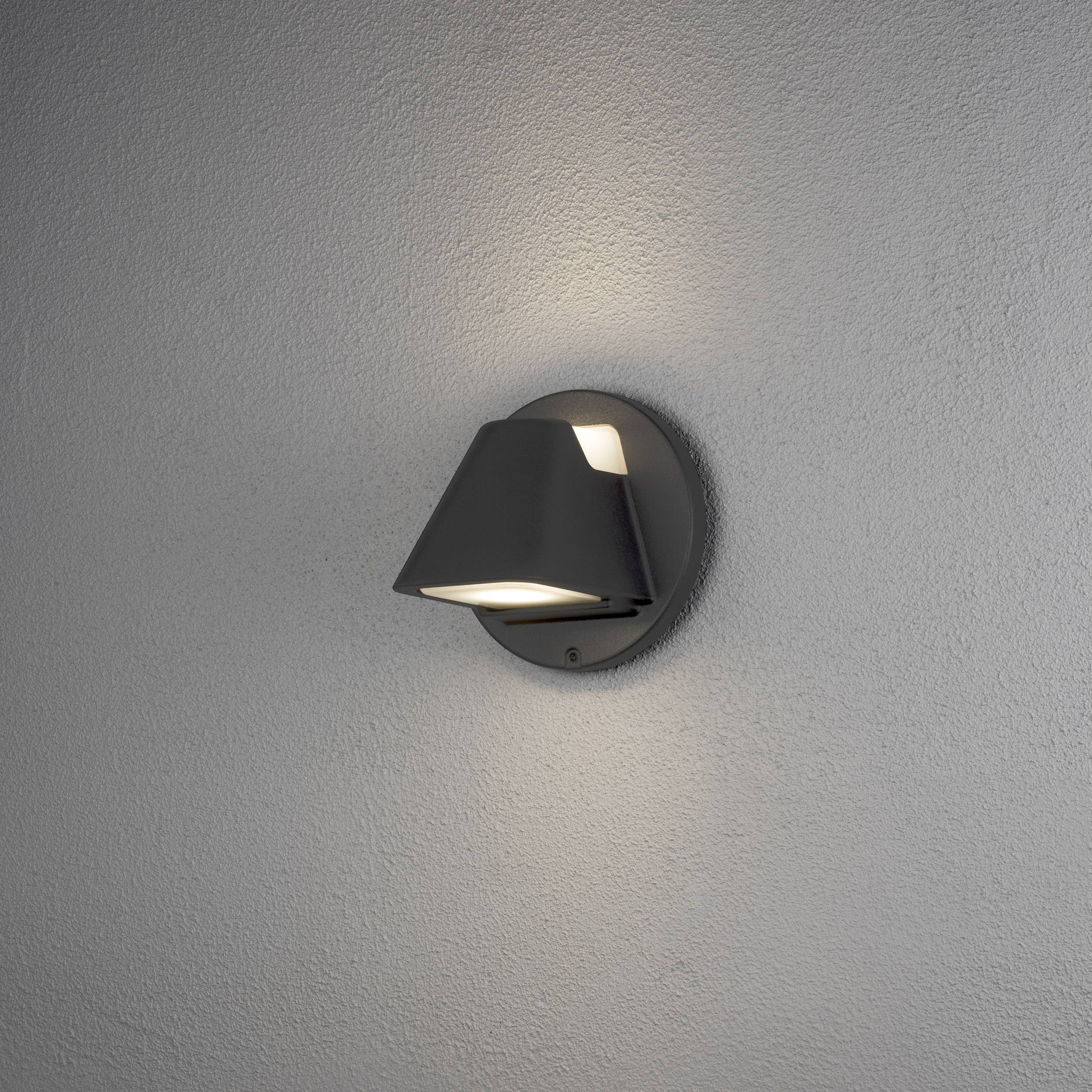 A wall lamp with a conical shade casts warm light on the grey wall and creates an atmospheric illumination.