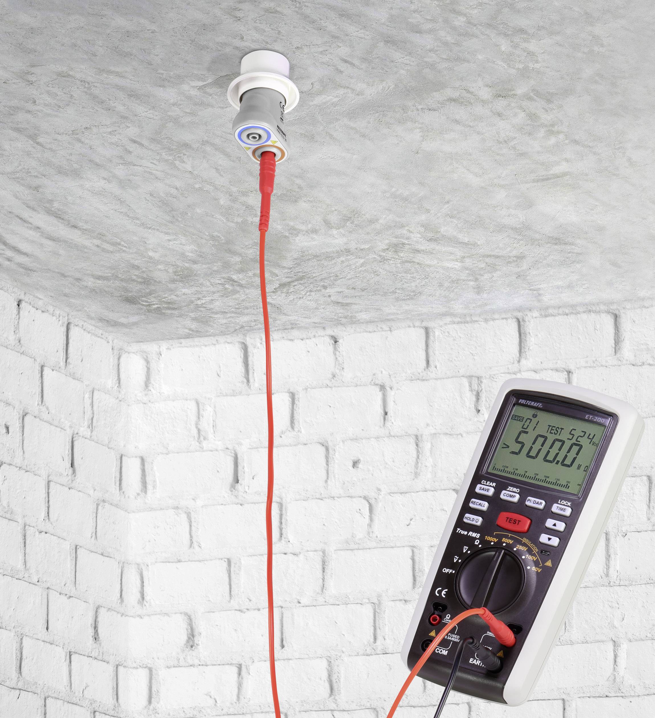 A multimeter is measuring the voltage at a ceiling socket. The display shows '500.0'. A red cable connects the two.