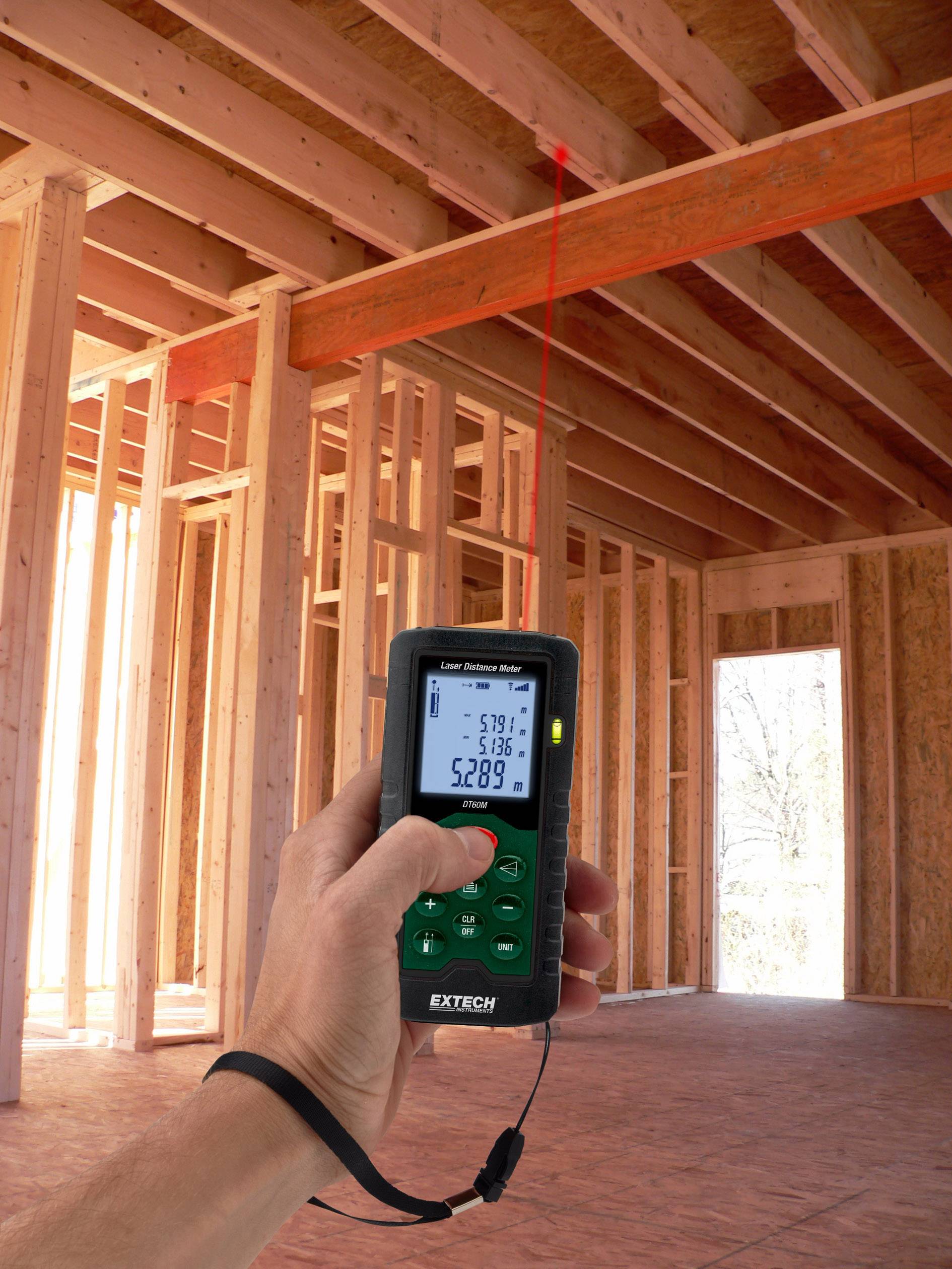 A handheld device is used to measure the distance to a red bar in an unfinished timber frame.