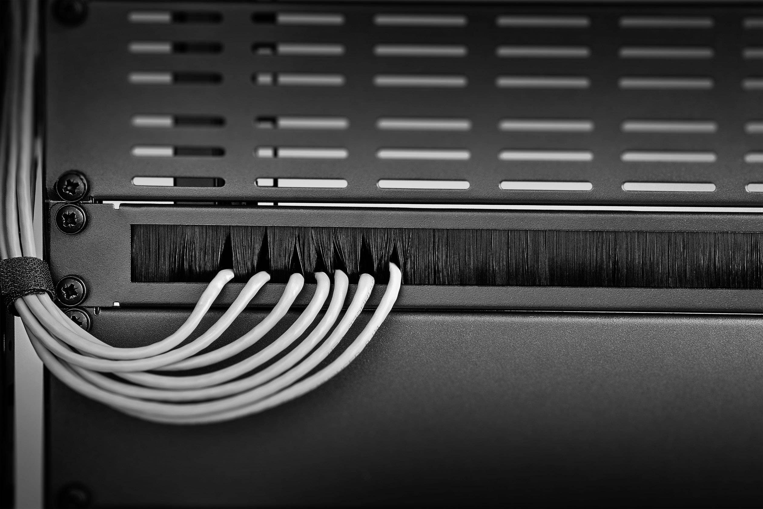 Cable management with multiple white cables routed through a brush strip into a rack, ensuring a tidy and secure cable installation.