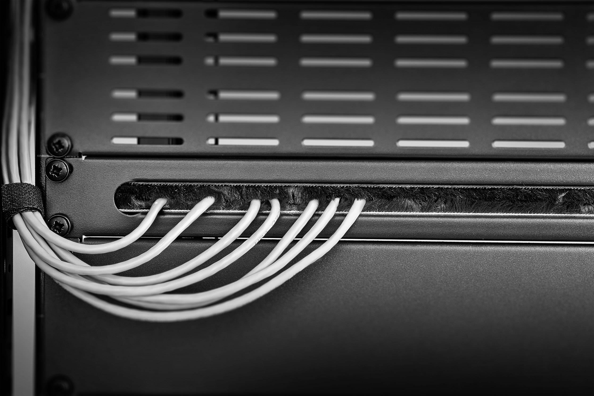 Black and white photograph of Ethernet cables leading into a server rack. The cables are neatly bundled and run to the left.
