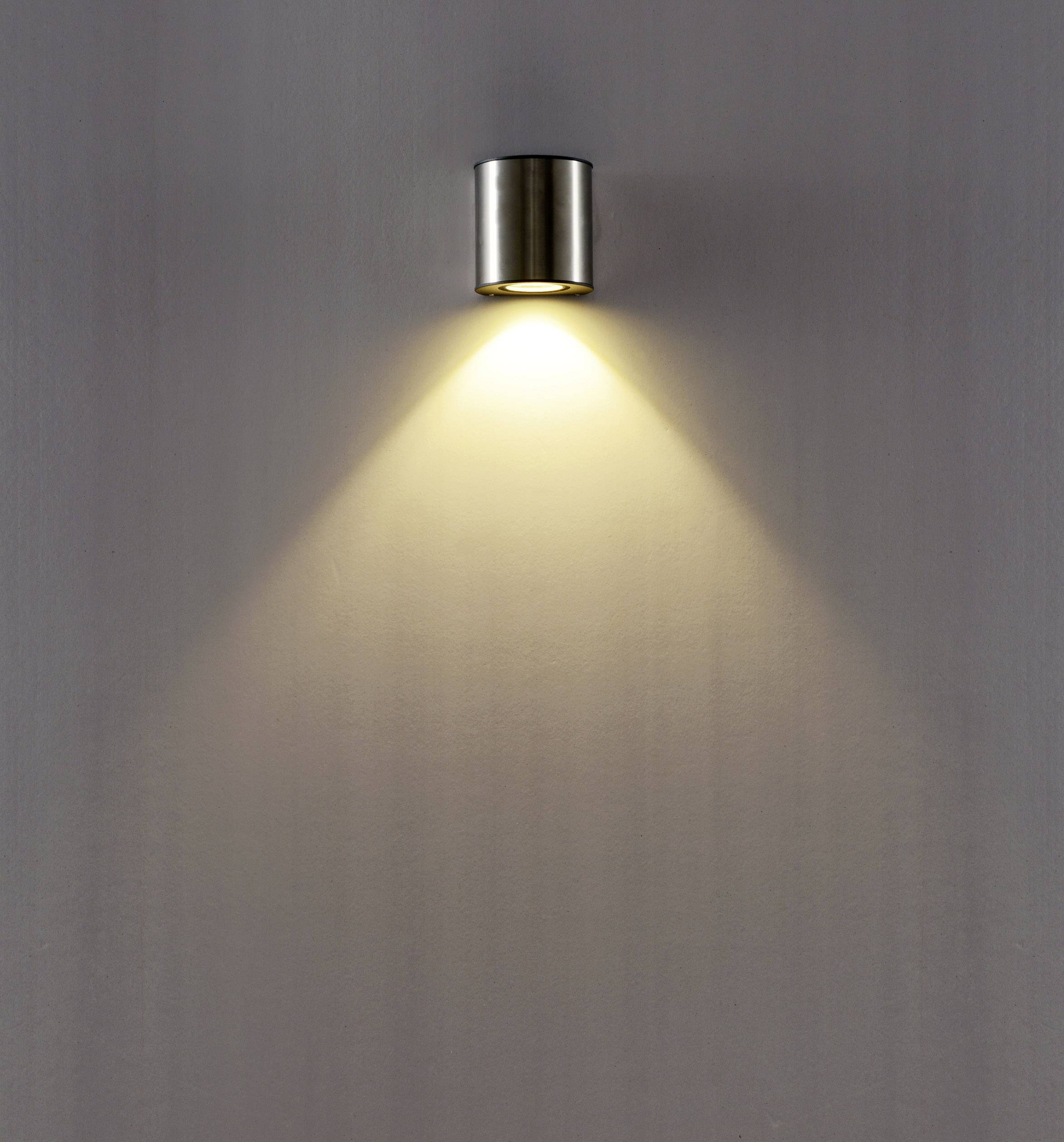 Wall light made of metal with a warm light beam spreading downwards onto a smooth wall. Minimalist design.