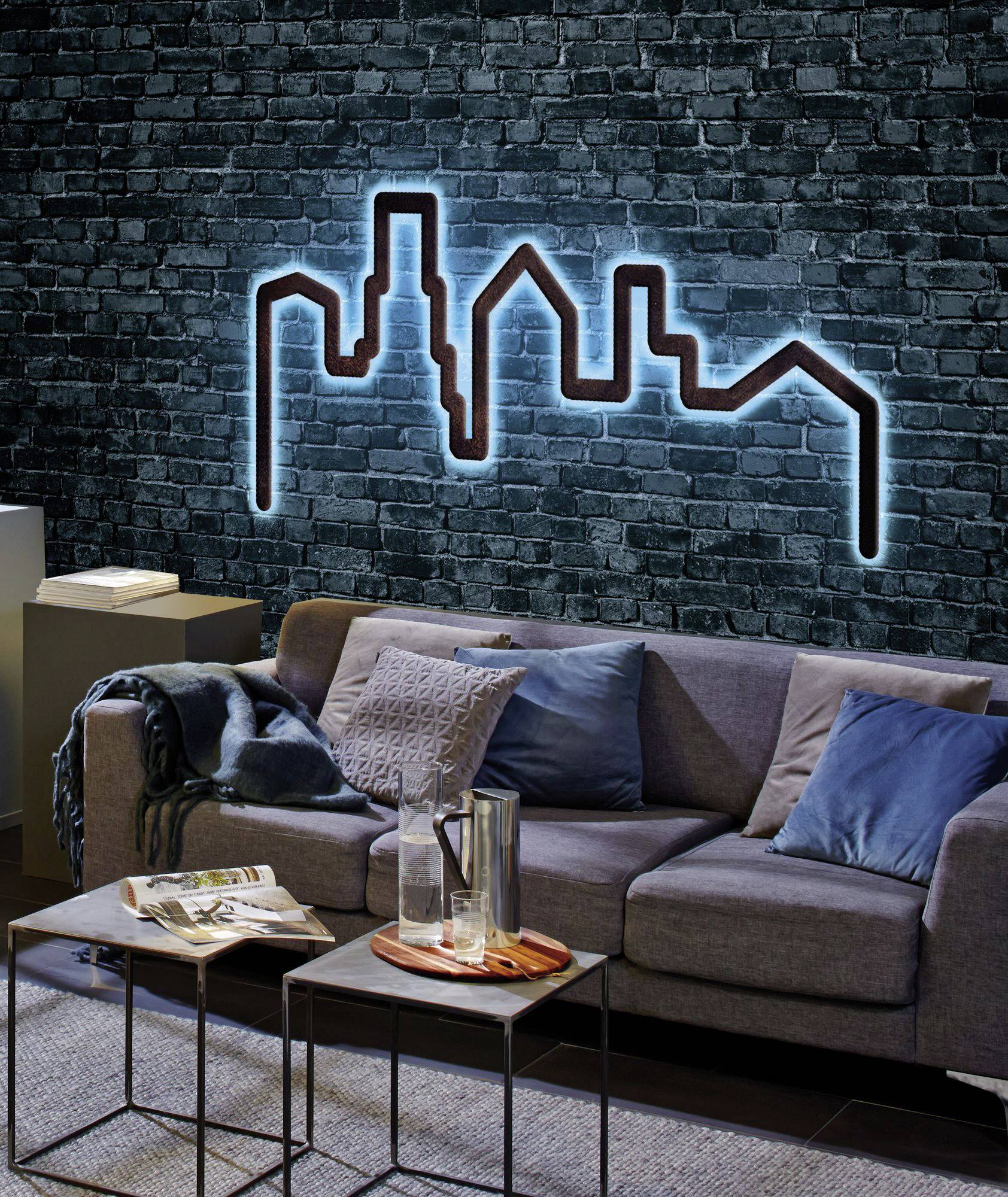 Sofa with cushions in front of a brick wall with a blue, illuminated skyline decoration.