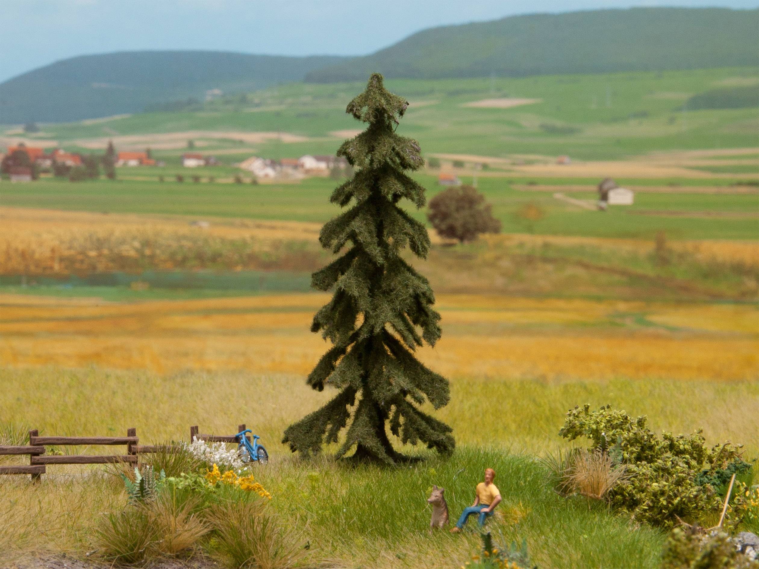 A miniature landscape with a large conifer in the centre, surrounded by fields and hills. Two figures are seated in the foreground on the right.