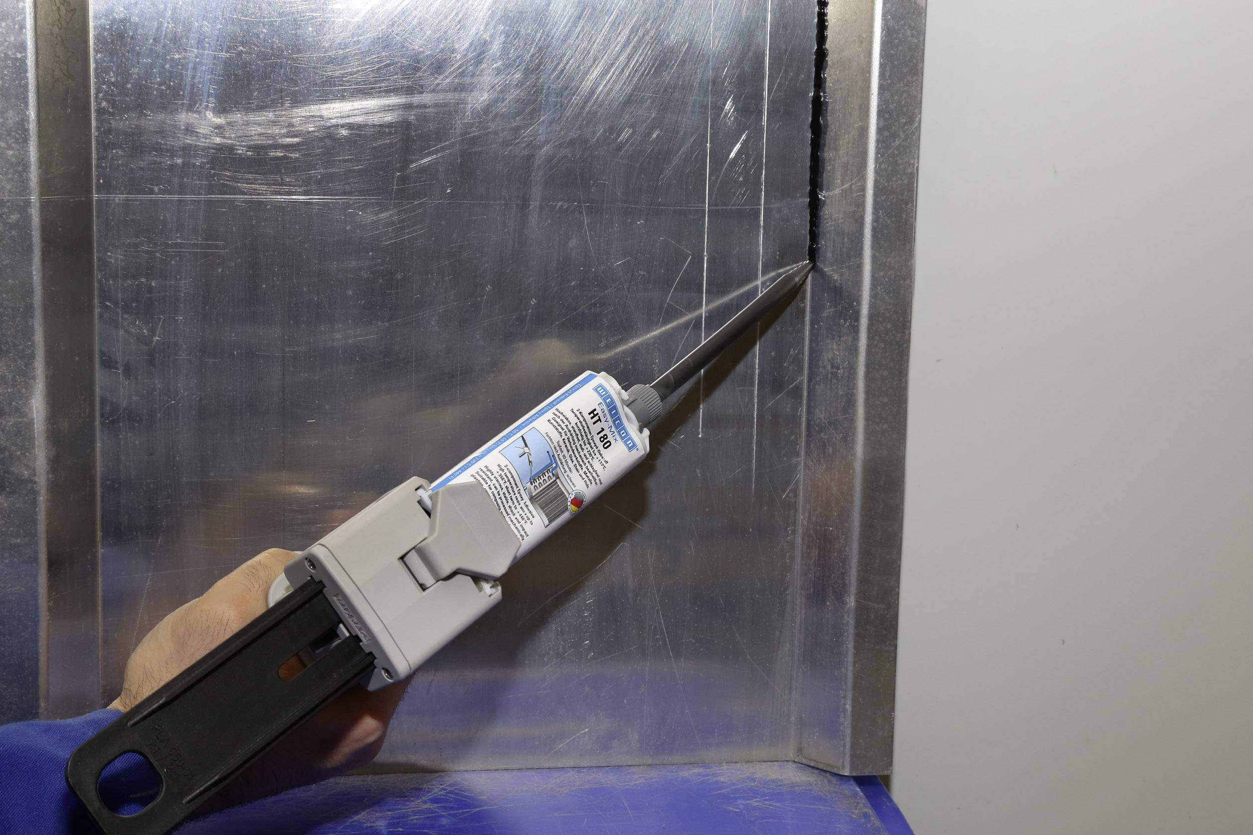 A person applies sealant to the corner of two metal plates.