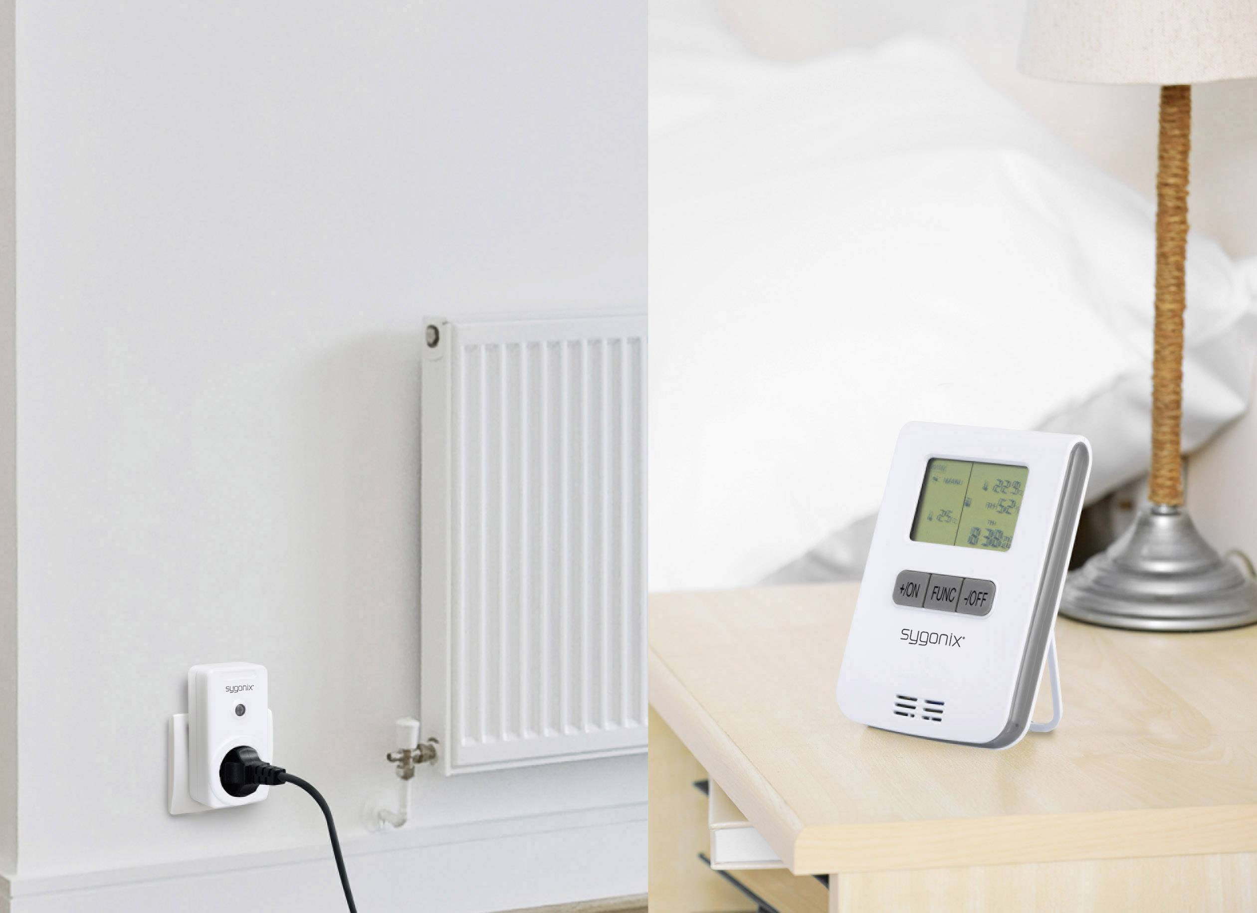 A radiator thermostat and a wall socket are shown beside a digital thermostat. A bed is visible in the background.