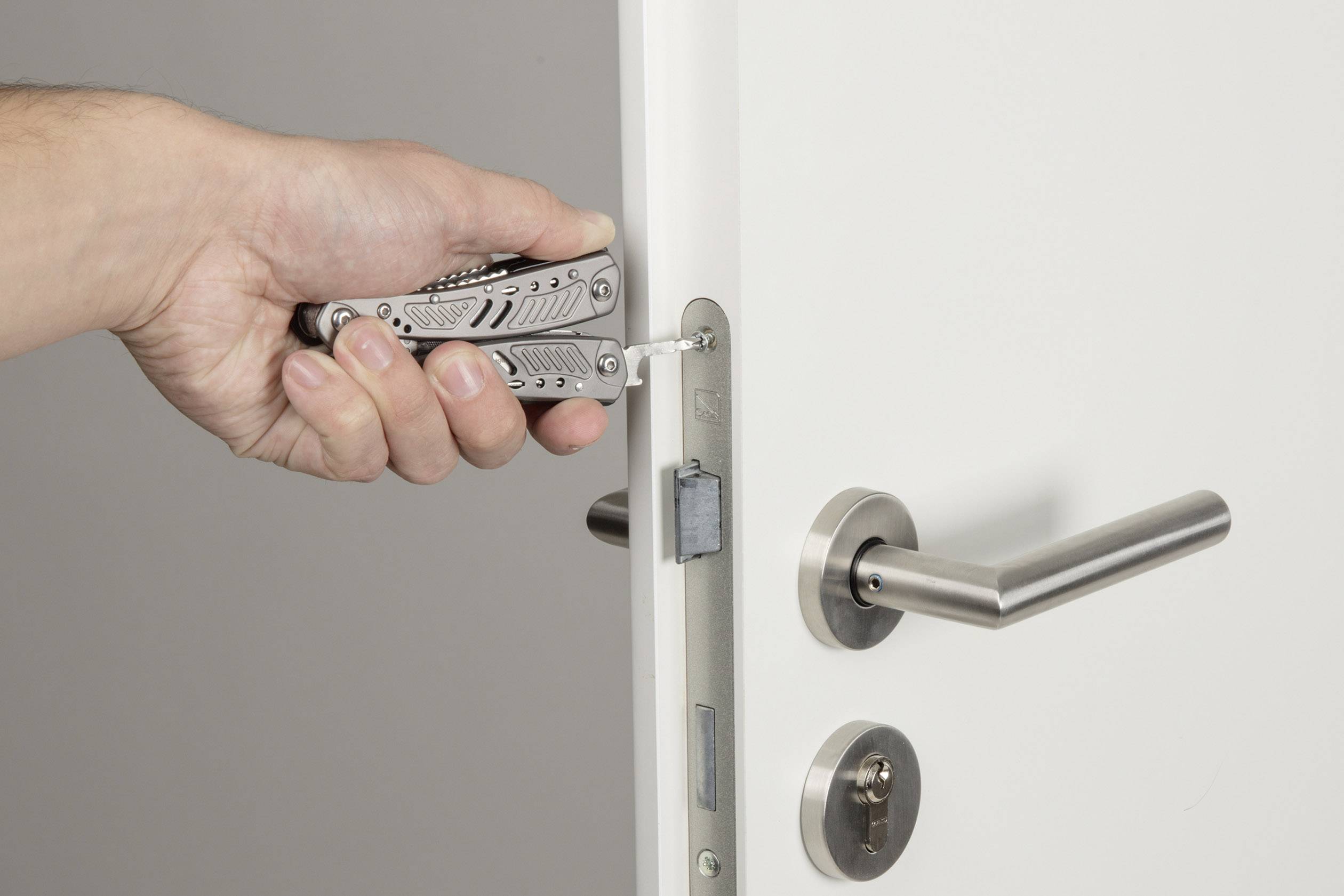 A hand is using a multi-tool to work on a door lock.