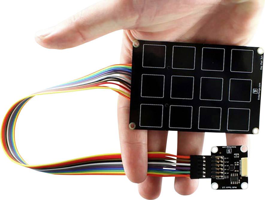 A hand is holding a capacitive touchpad module with nine squares and rainbow cables, which is used for electronic projects.