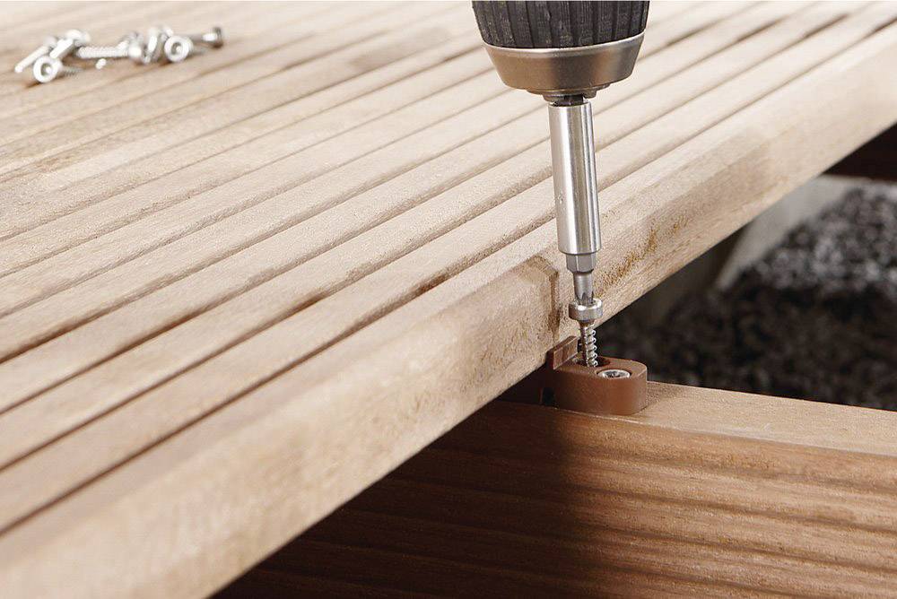 A close-up shows a cordless drill driving a screw into a wooden board. Further screws are visible in the background.