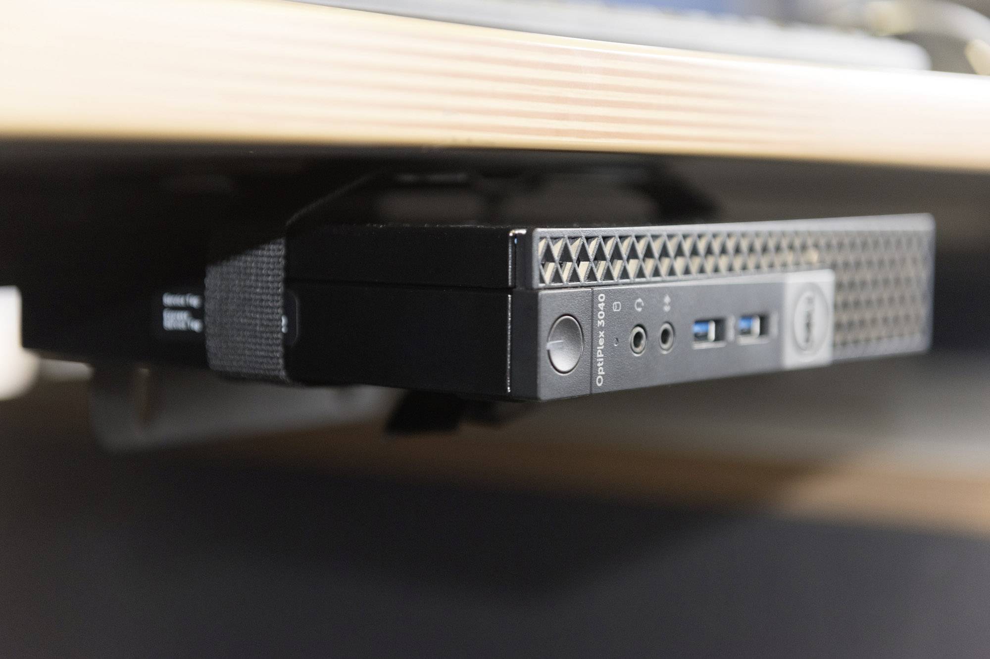 A compact computer is mounted under a table. It has various connections, including USB ports.