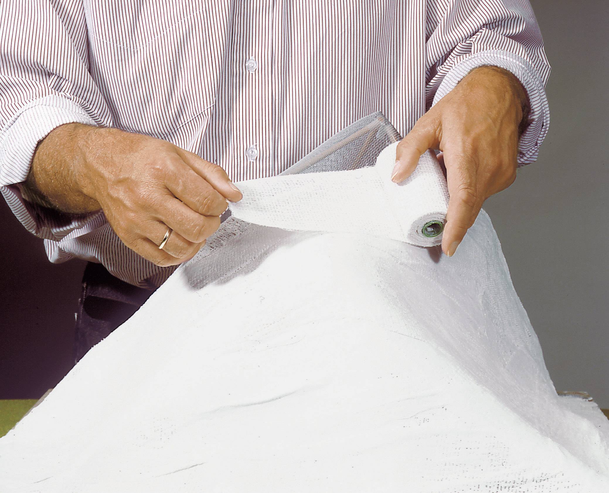 A person is applying a plaster cast around an arm. The focus is on the hands and bandaging material.