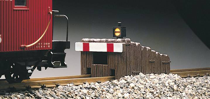 A red goods wagon on a track in front of a buffer stop with a red stop light. Gravel and a dark background.
