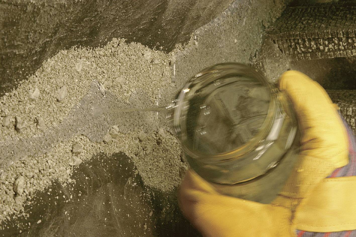 A person is pouring water from a glass onto a concrete surface, likely to observe a reaction or clean the area.