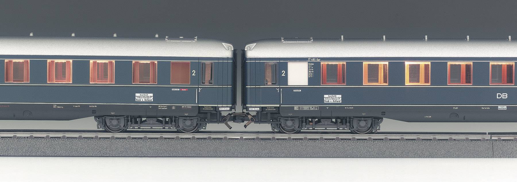 Two blue railway carriages, connected on a track, with orange-illuminated windows.