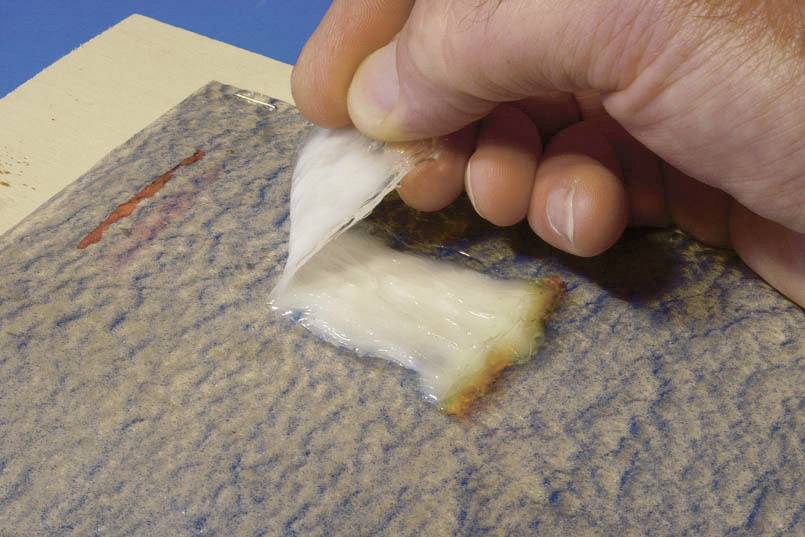 A hand is peeling a transparent layer from a blue surface, which could be part of a cleaning or preservation process.