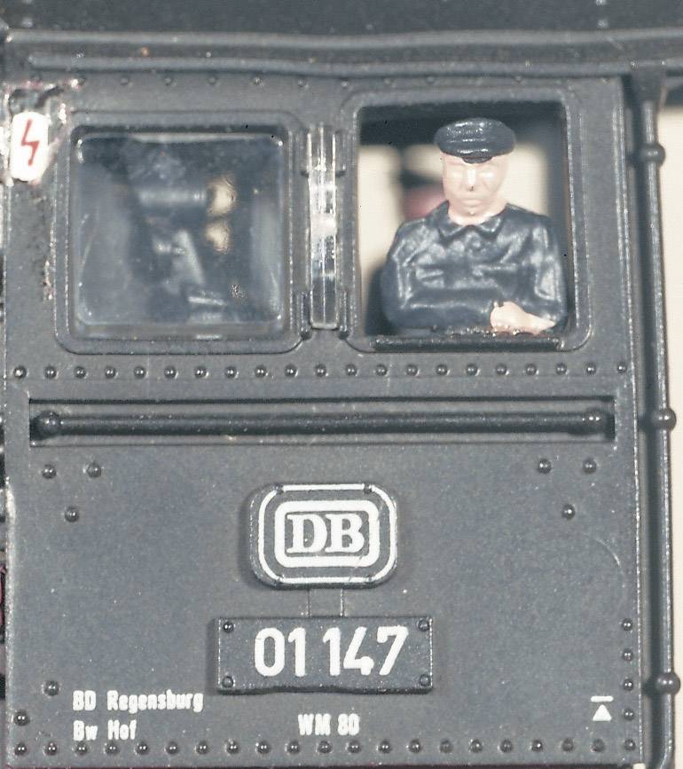 A miniature model railway with the number '01147' and 'DB' logo. A miniature figurine train driver looks out from the cab.
