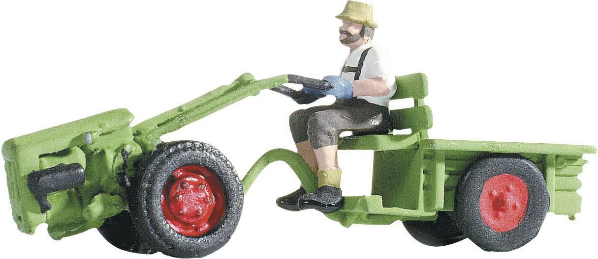 A model of a green tractor with a trailer. A man wearing a hat is sitting at the wheel. The tractor and trailer have red wheels.
