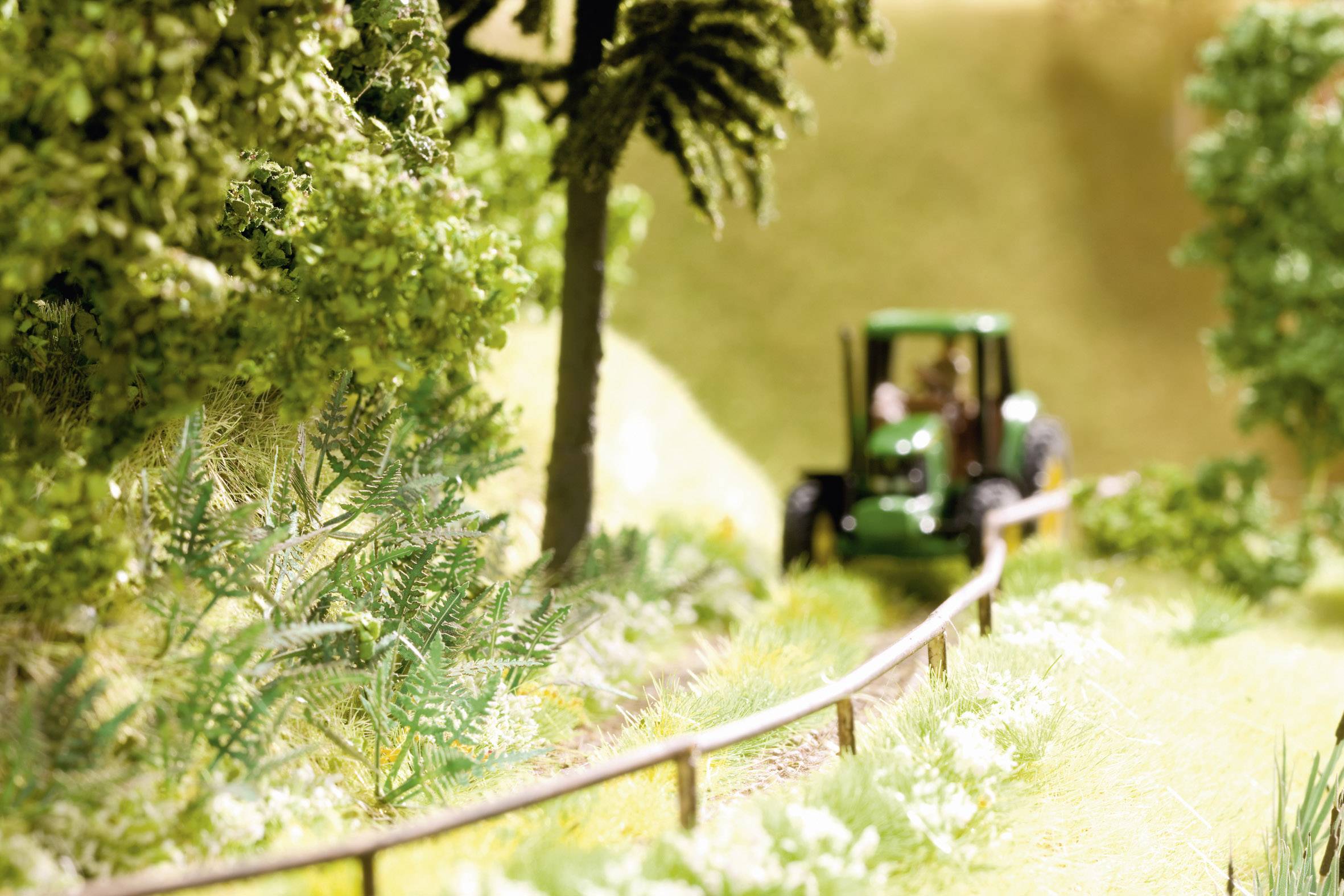 A small tractor is driving along a narrow path through a green, wooded landscape.