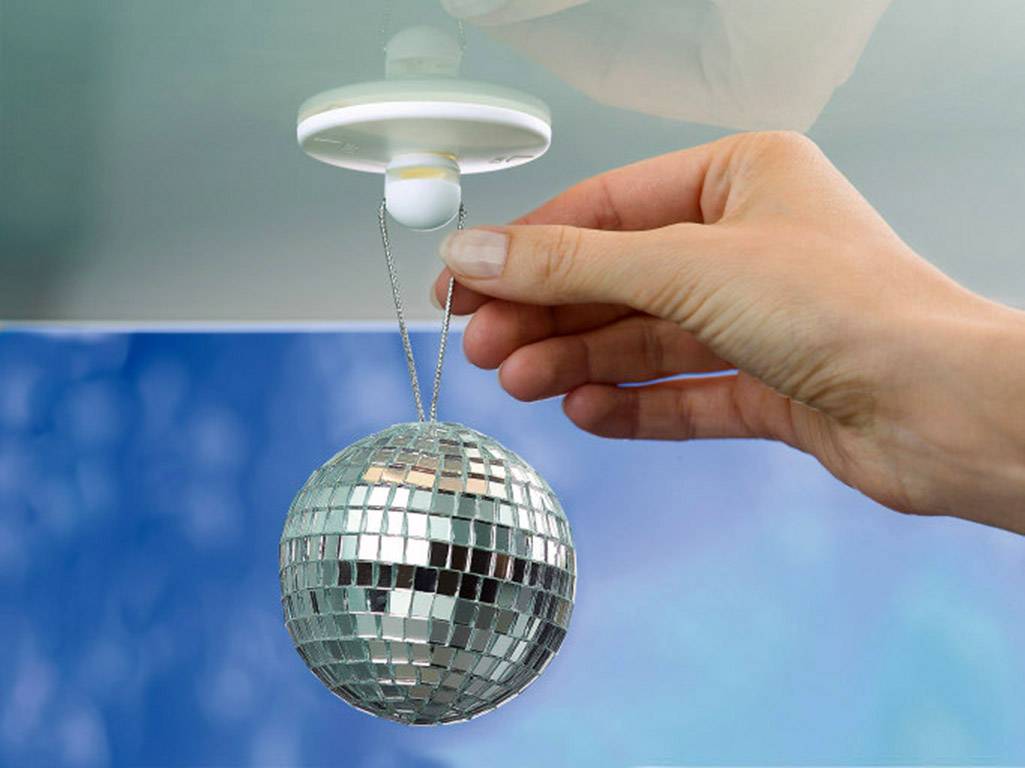 A hand hangs a small disco ball from a ceiling fitting. The surroundings are blue and out of focus, which emphasises the ball.