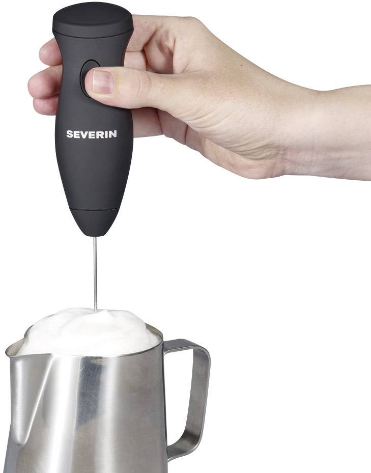 A hand is holding an electric milk frother over a silver jug of frothed milk.