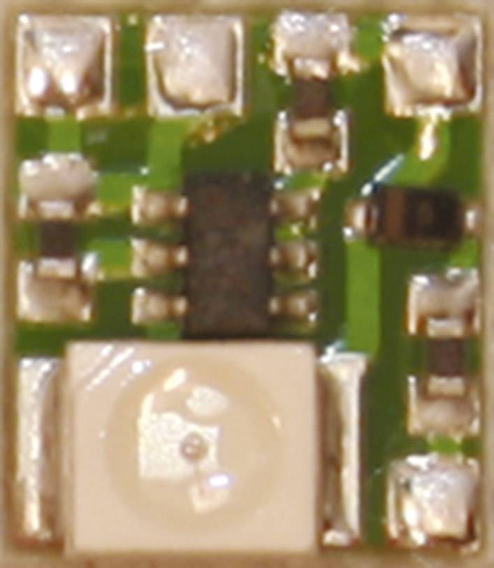Close-up of a small electronic component on a circuit board with visible circuitry and a square chip in the bottom left.
