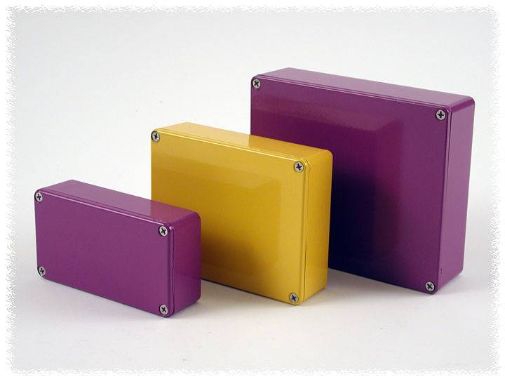 Three rectangular, coloured metal boxes in purple and yellow of varying sizes are placed side by side on a white surface.