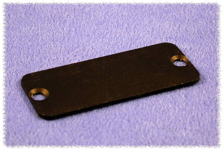 Rectangular black metal plate with two holes at the ends, resting on a blue fabric background.Note: This translation is already in British English, so no significant changes were needed.