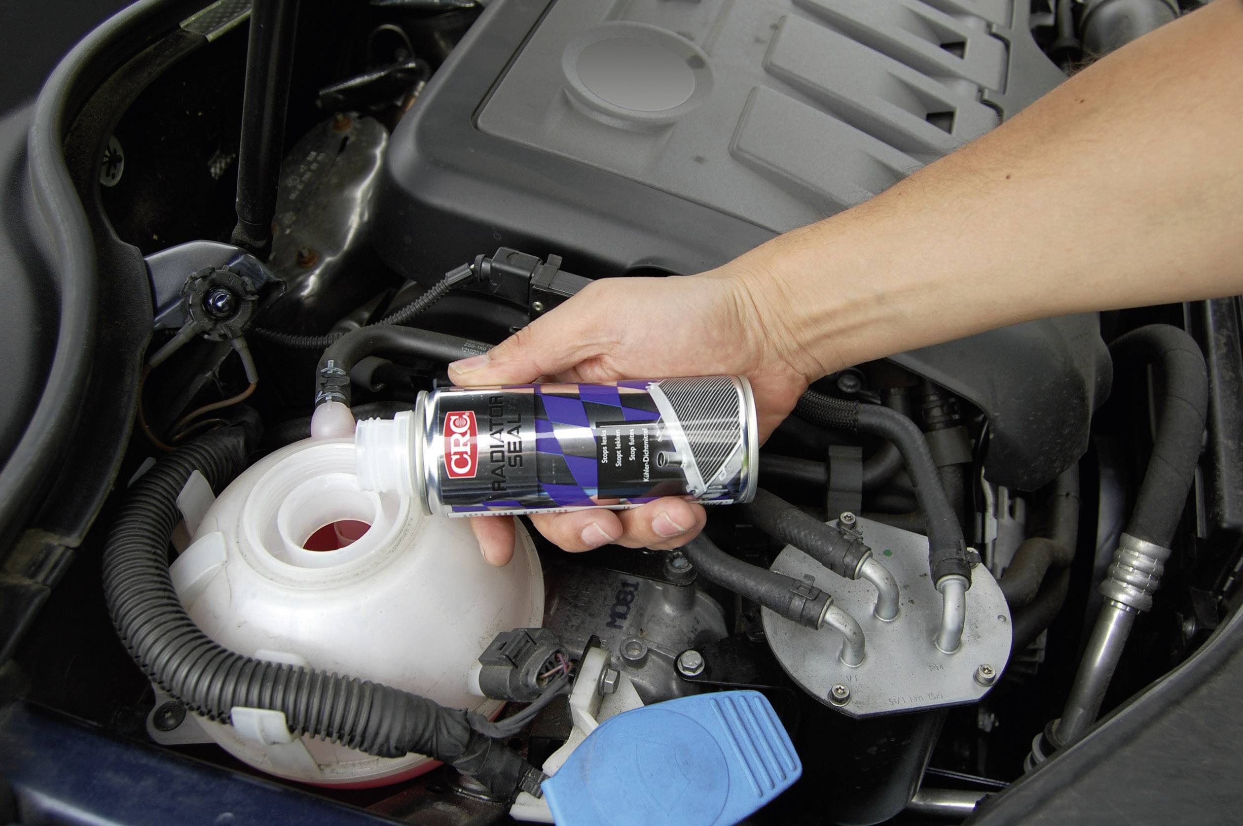 A hand holds a bottle of coolant and pours it into the coolant reservoir of a car to protect the engine.