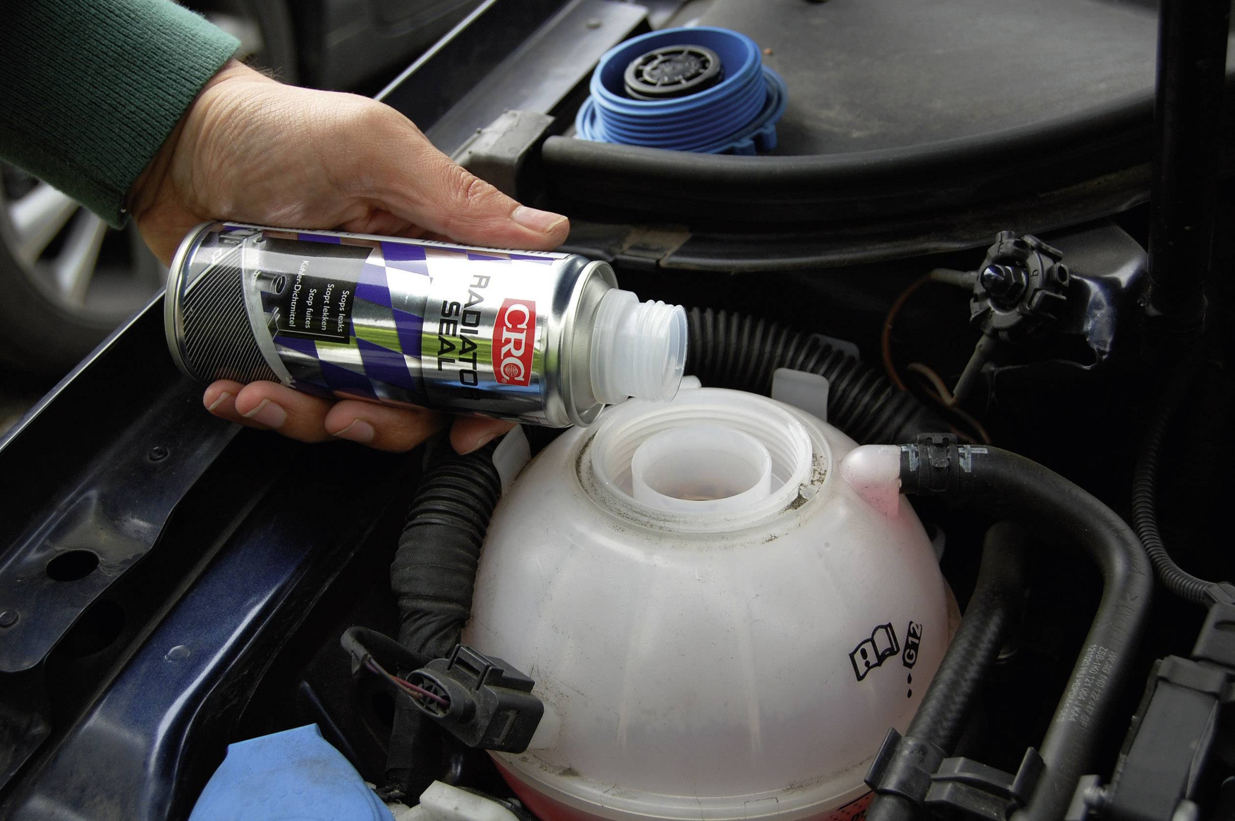 A person is topping up the coolant in a car's expansion tank. The tank is already partially filled.