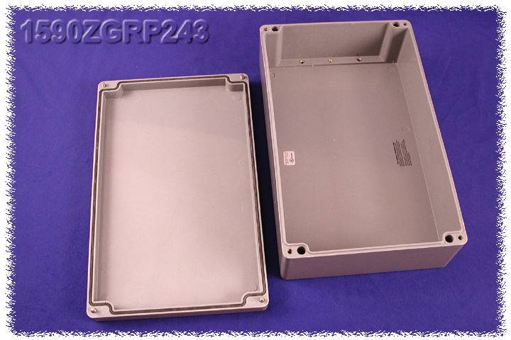 Grey rectangular enclosure, semi-open, on a blue background. On the left is the lid, on the right is the base. Top left reads '1590ZGRP243'.