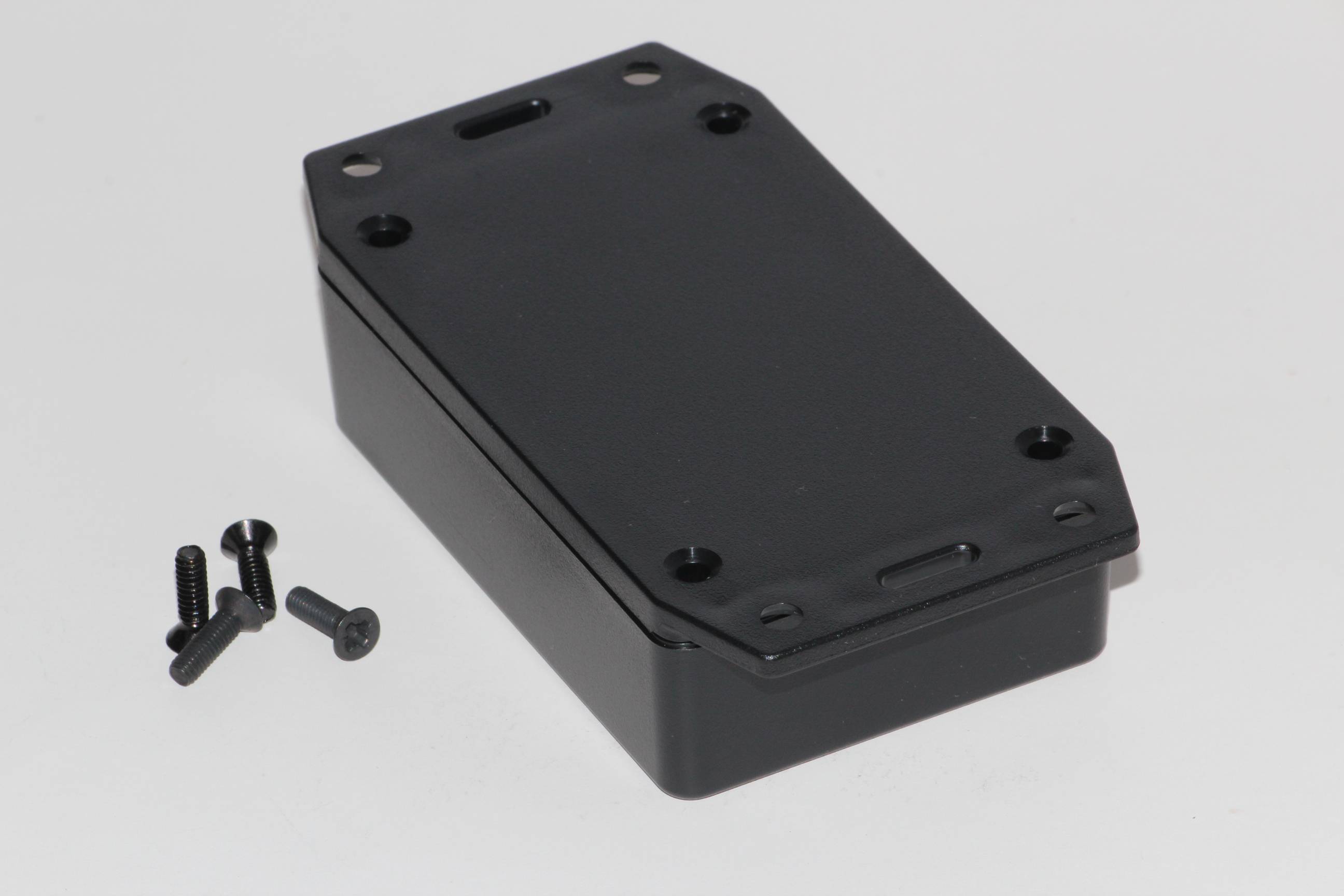 A rectangular, black electronic enclosure with four screws beside it, on a white background.