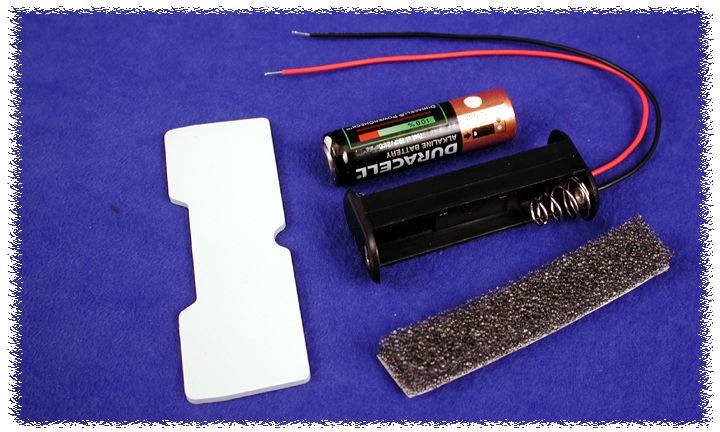 Components of a battery compartment: Battery case with spring, AA battery, foam strip and a white plastic part on a blue background.