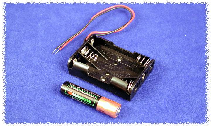 Battery holder for two AA batteries with a single loose AA battery, lying on a blue surface. Wires are attached to the holder.