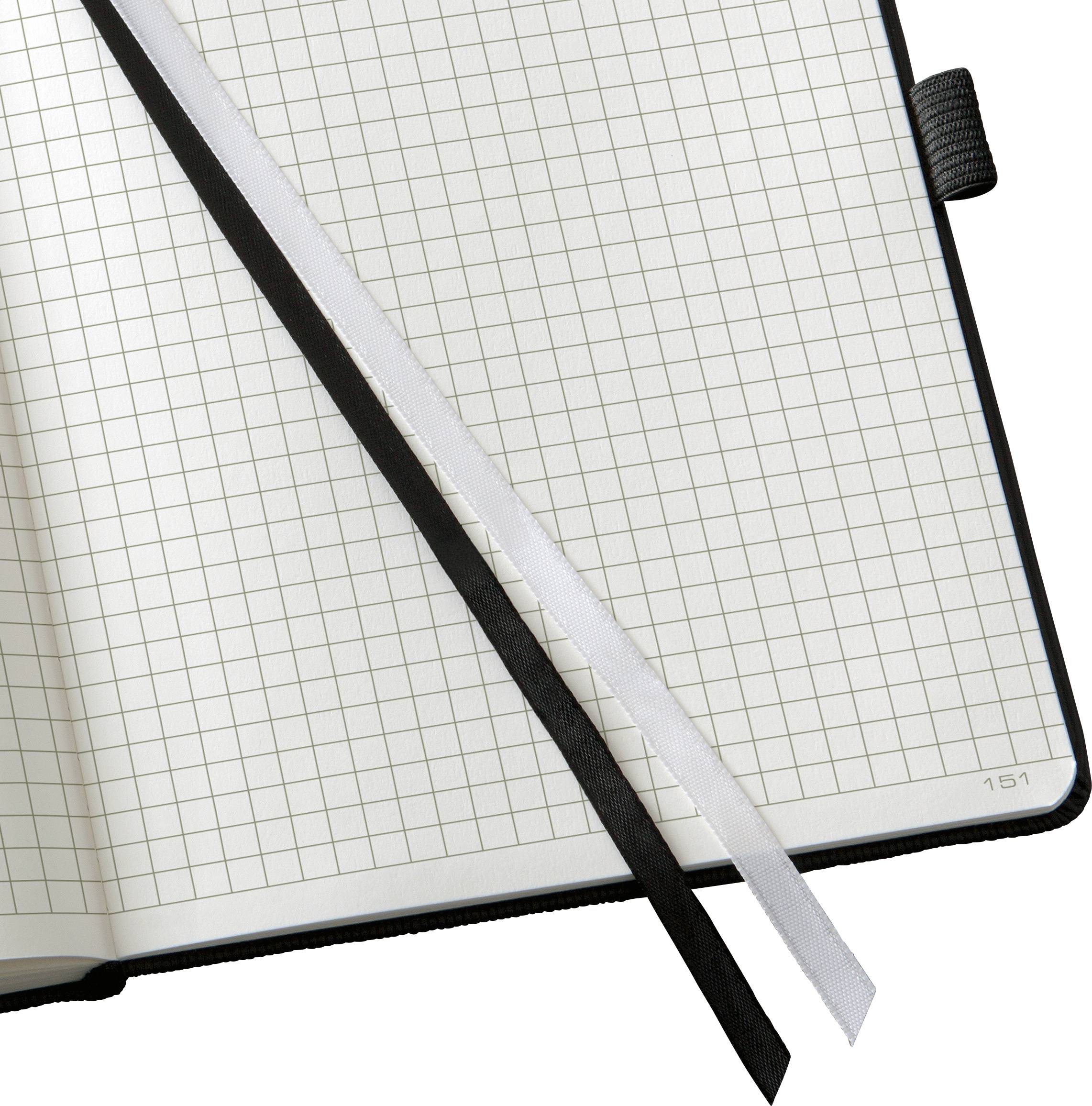 An open notebook with squared pages. Two fabric bookmarks, one in black and one in white, are resting on the pages.