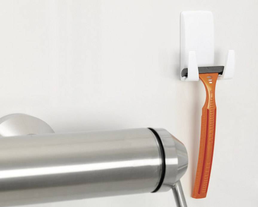 An orange razor hangs on a white wall holder next to a chrome towel rail.