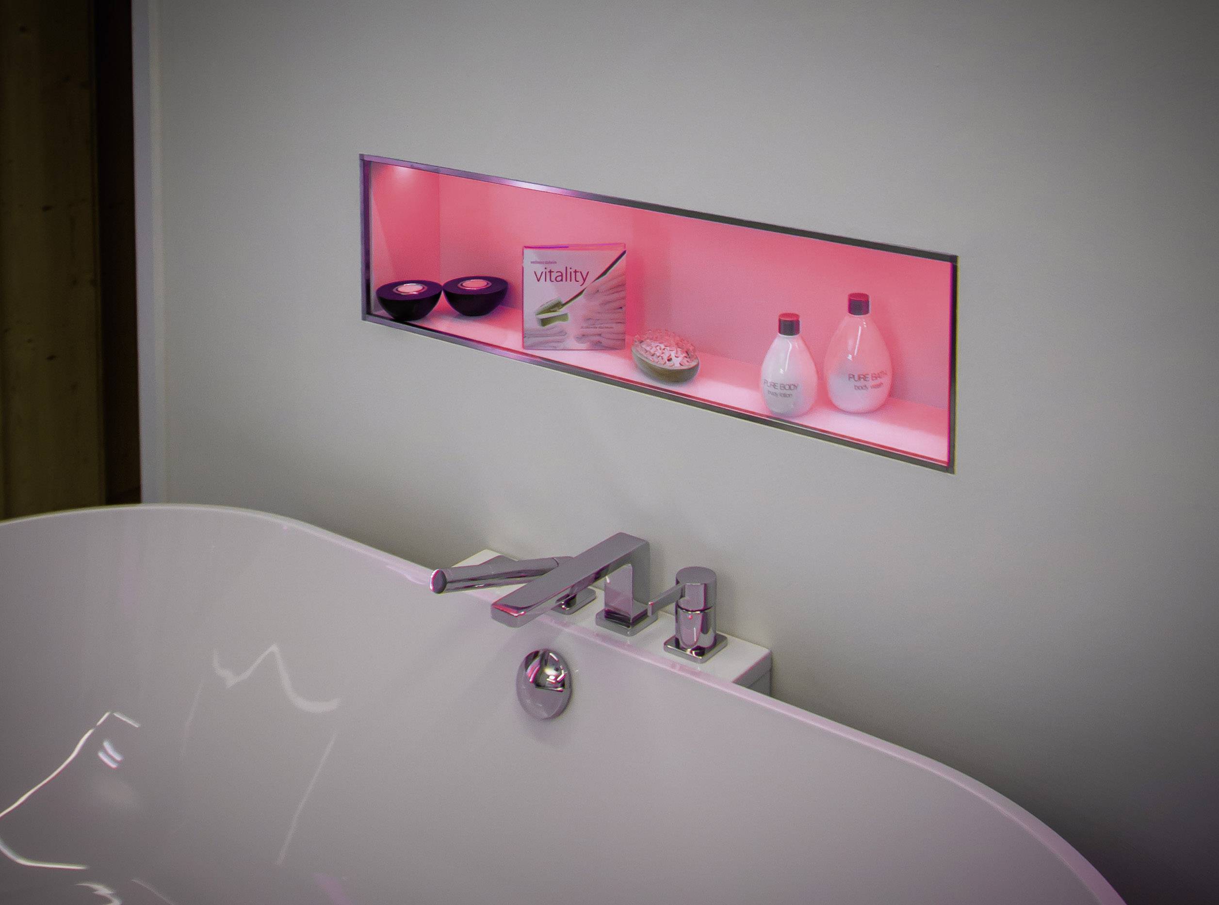 A white bath tub with a contemporary tap. In the background, a shelf with red lighting, containing toiletries and bowls.