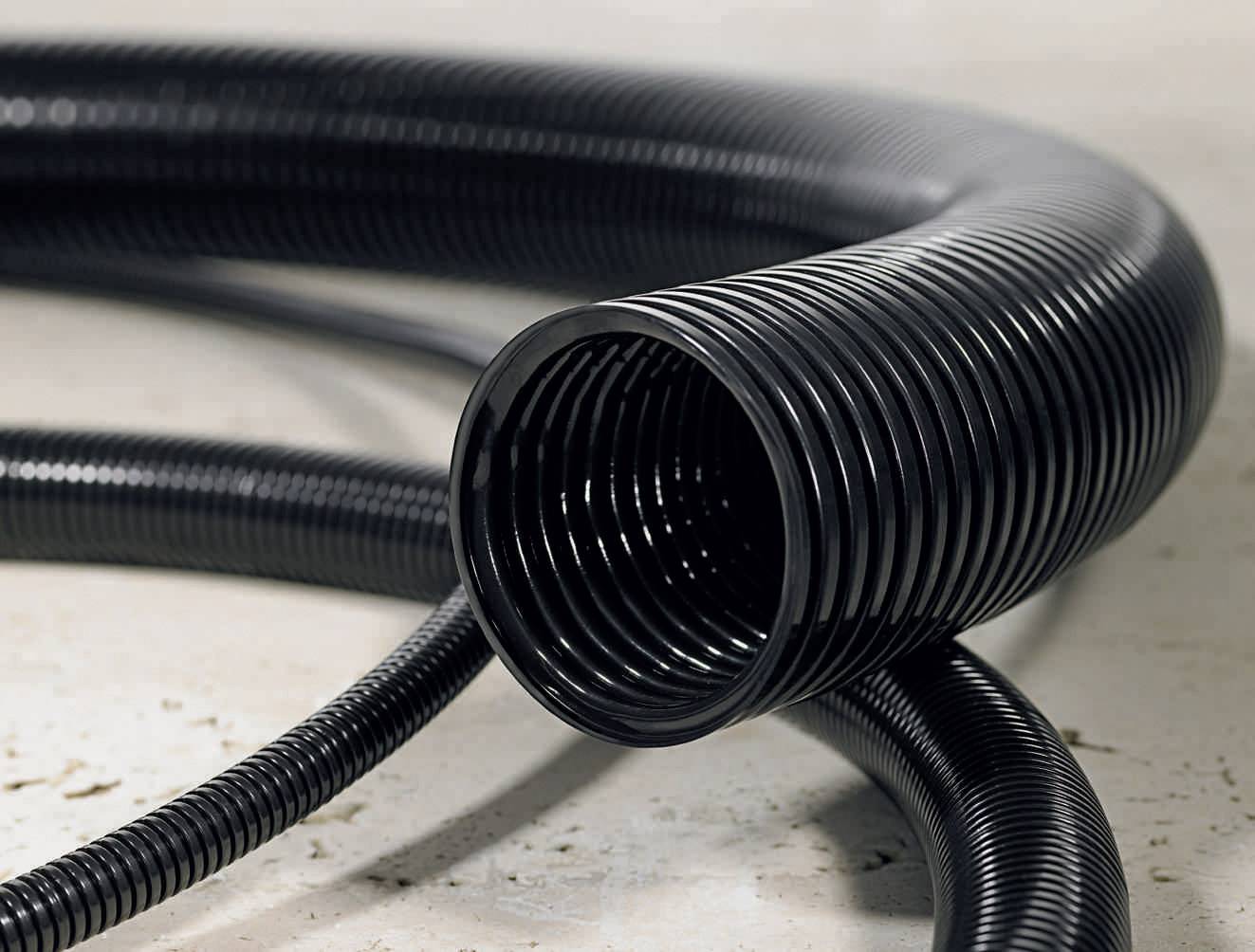 Black, corrugated plastic hose, coiled on a light surface. Used for flexible cable or pipe routing.