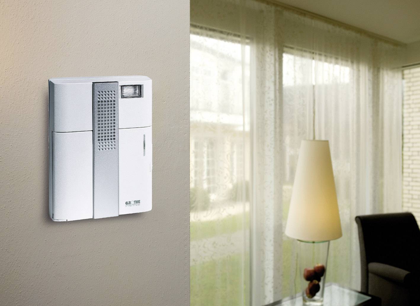 A modern intercom system mounted on the wall of a living room, with a window in the background illuminating the space.